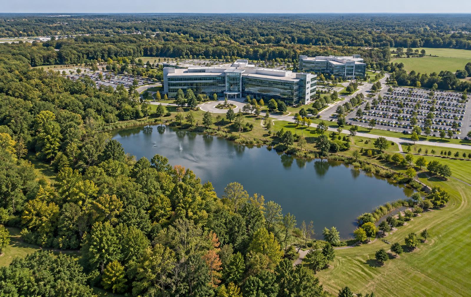Aerial daytime view of a corporate facility with large grounds including wooded area, water and open acreage